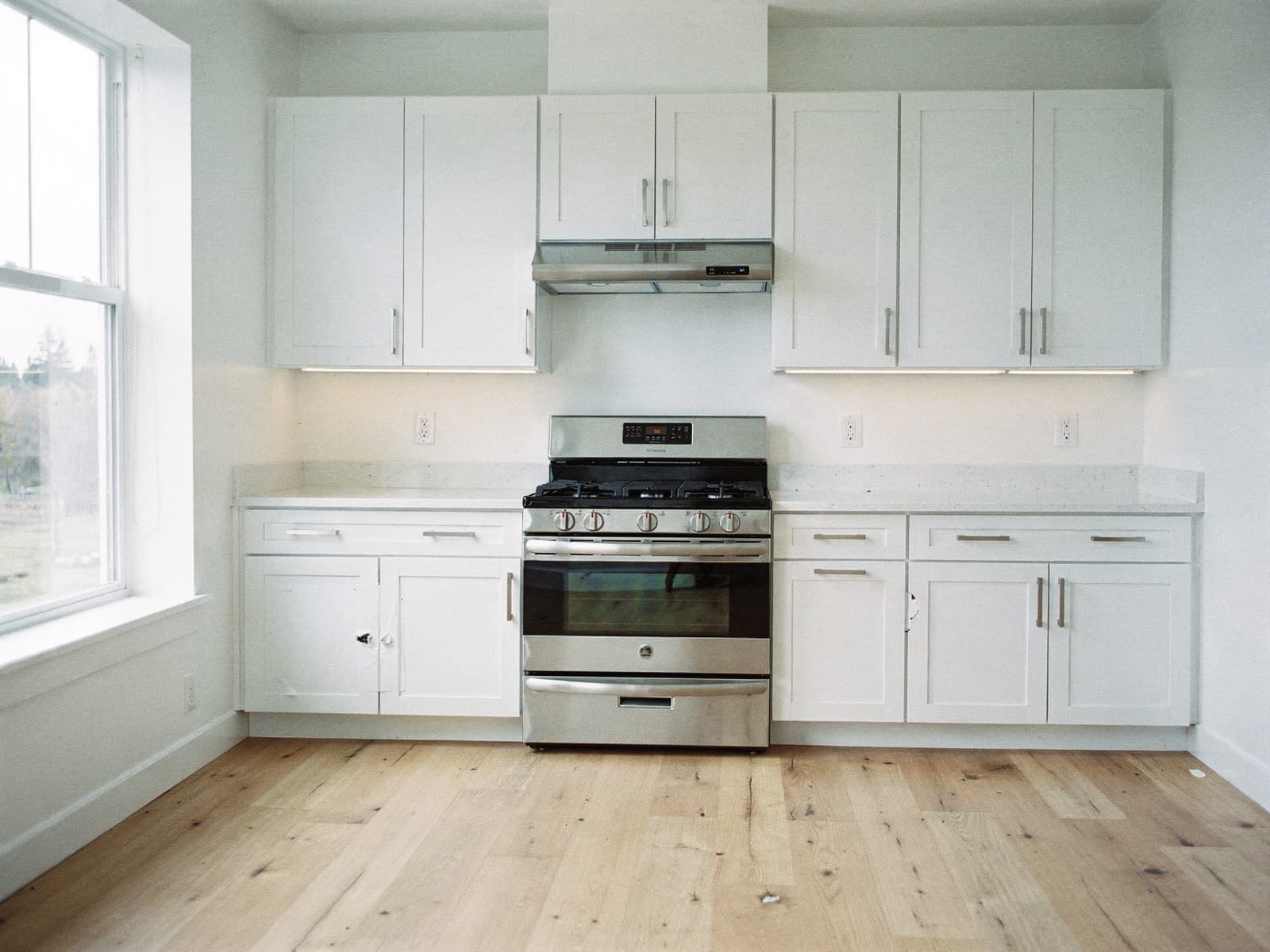Empty apartment kitchen with bare countertops and open cabinet, daylight across the counter